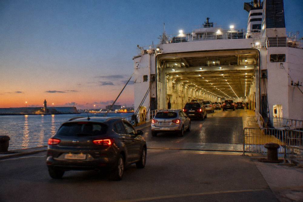 Ferry vehicle deck seen from the quay with rows of cars driving in under floodlights at evening
