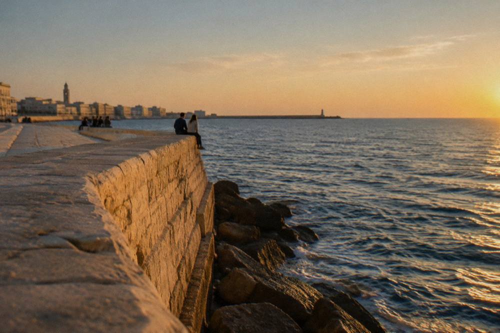 Distant people sitting on the broad top of a pale limestone sea wall above the open Adriatic in soft warm light