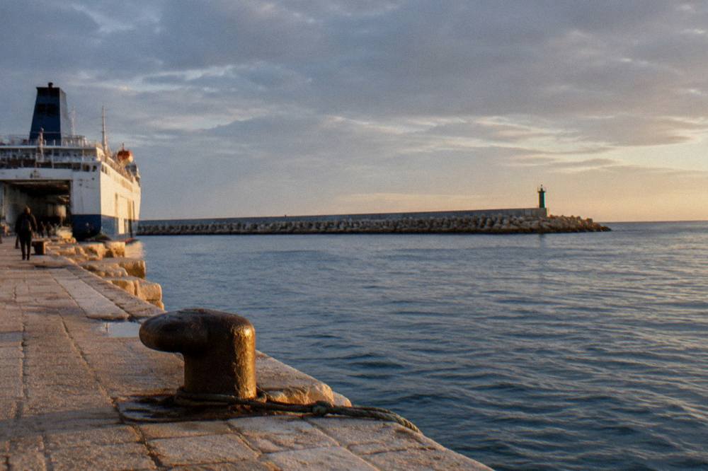 Long breakwater of concrete blocks with a small beacon at its end above the open Adriatic