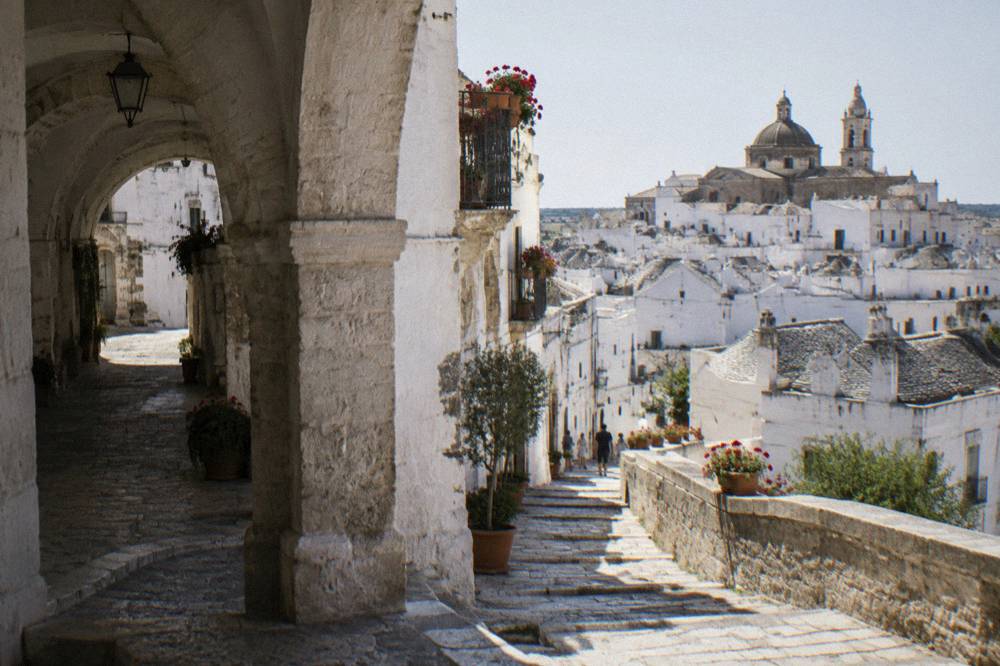 Whitewashed circular hill town with balconies of geraniums, stone staircases and a church dome