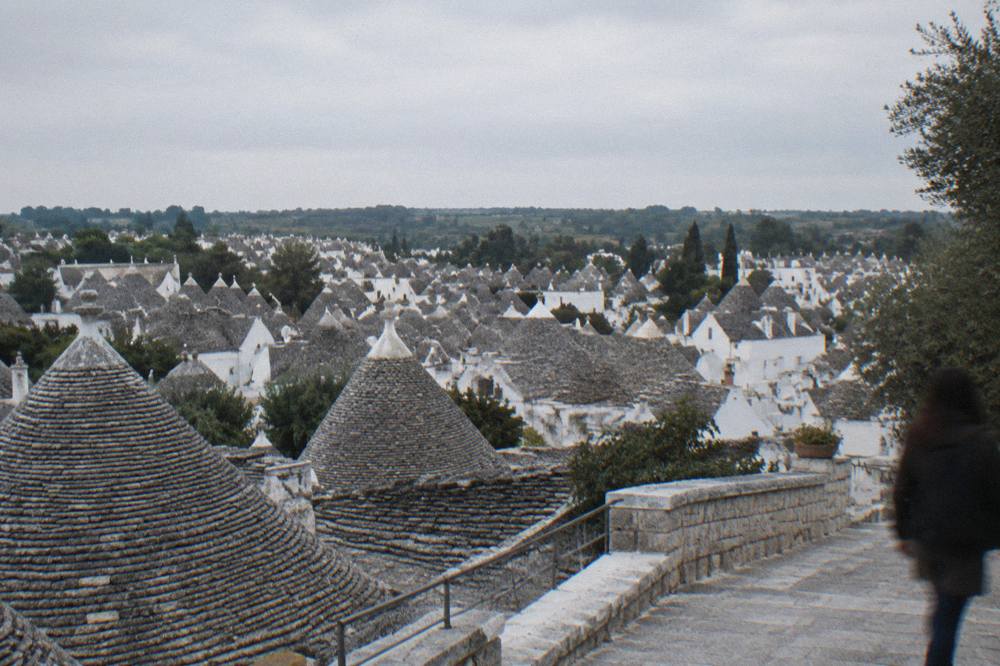 Wide view over a dense cluster of grey conical stone roofs from a raised belvedere