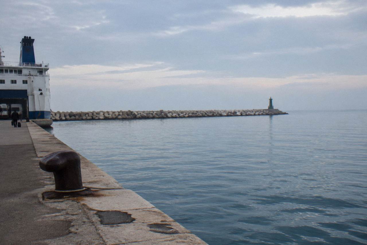 Long breakwater of concrete blocks with a small beacon at its end above the open Adriatic