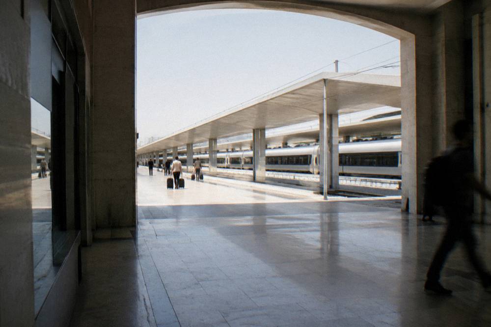 Large pale railway station with a long concourse, distant travellers with suitcases and plain trains at the platforms