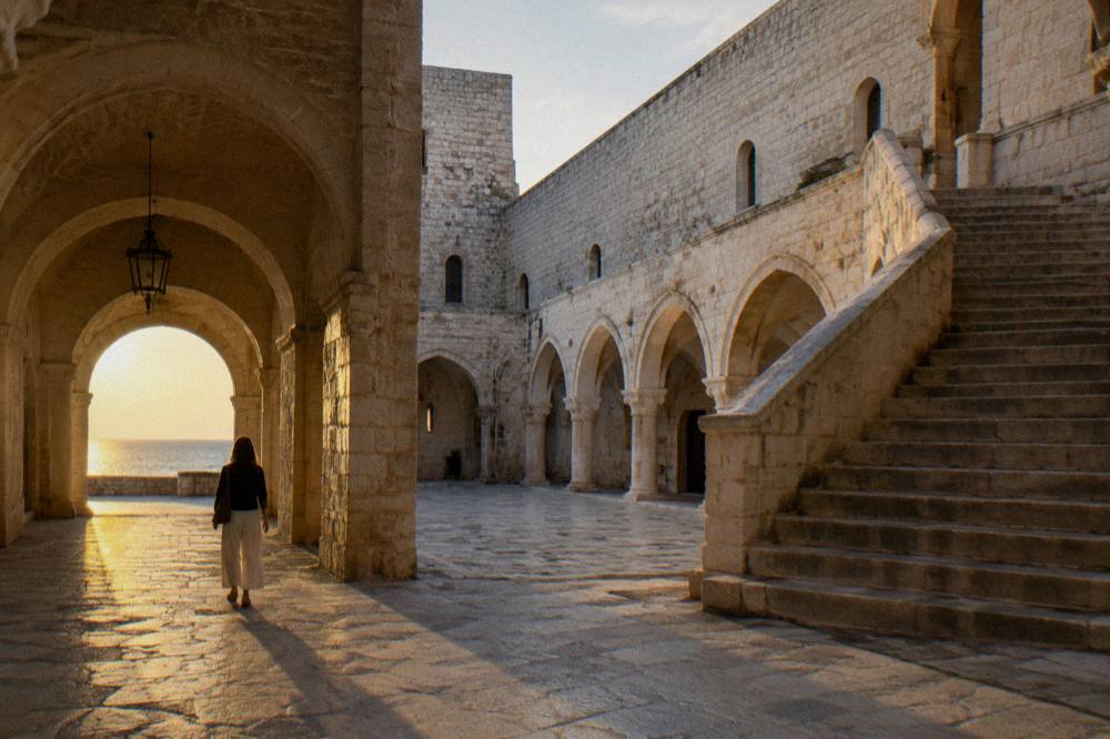 Inner courtyard of a medieval castle with a pale stone arcade, a broad staircase and a vaulted passage