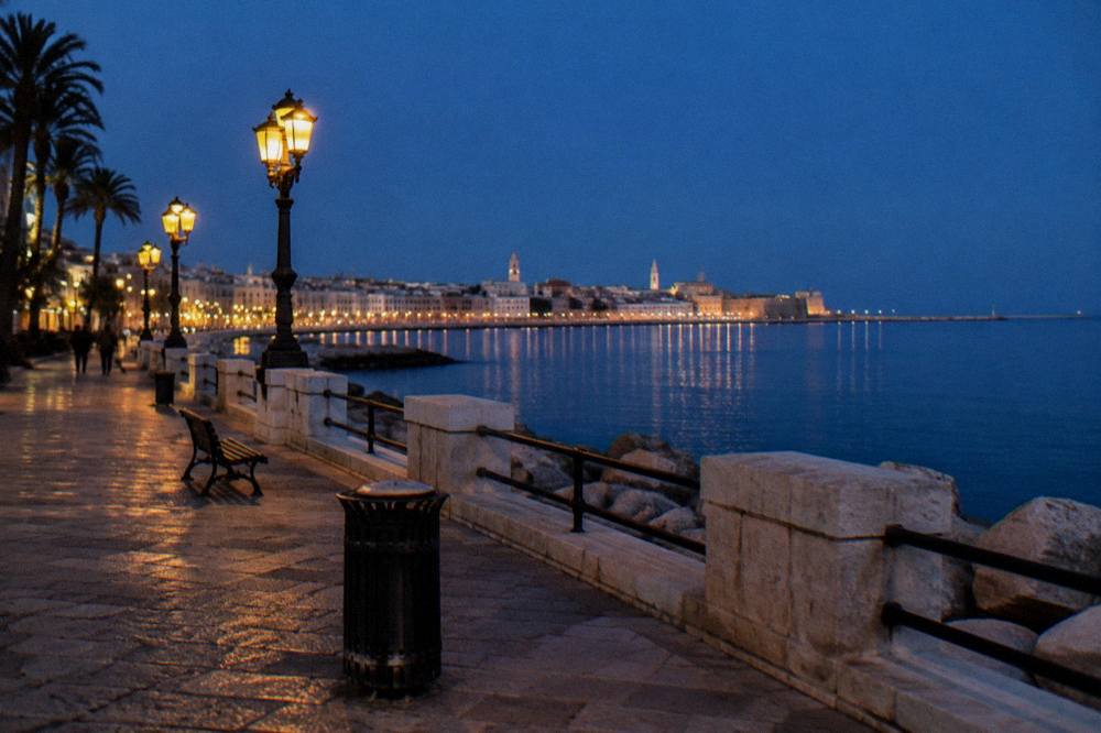 Seafront promenade at blue hour with lit street lamps and the lights of the old town across the bay