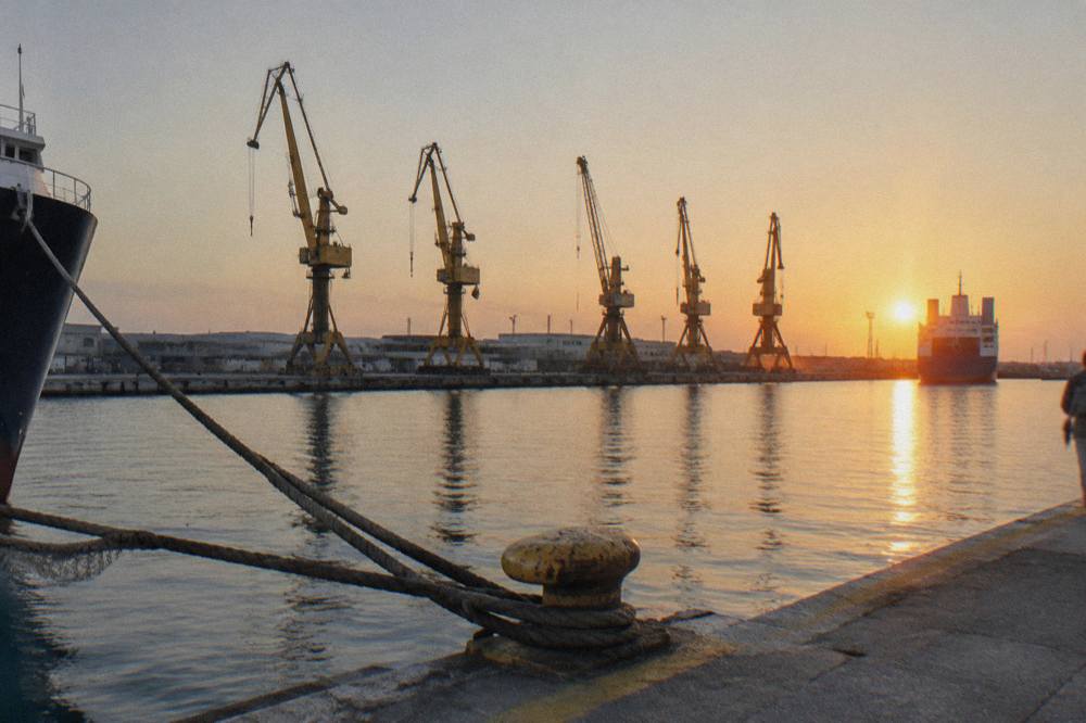 Row of harbour cranes behind a calm commercial dock with ropes and bollards in the foreground