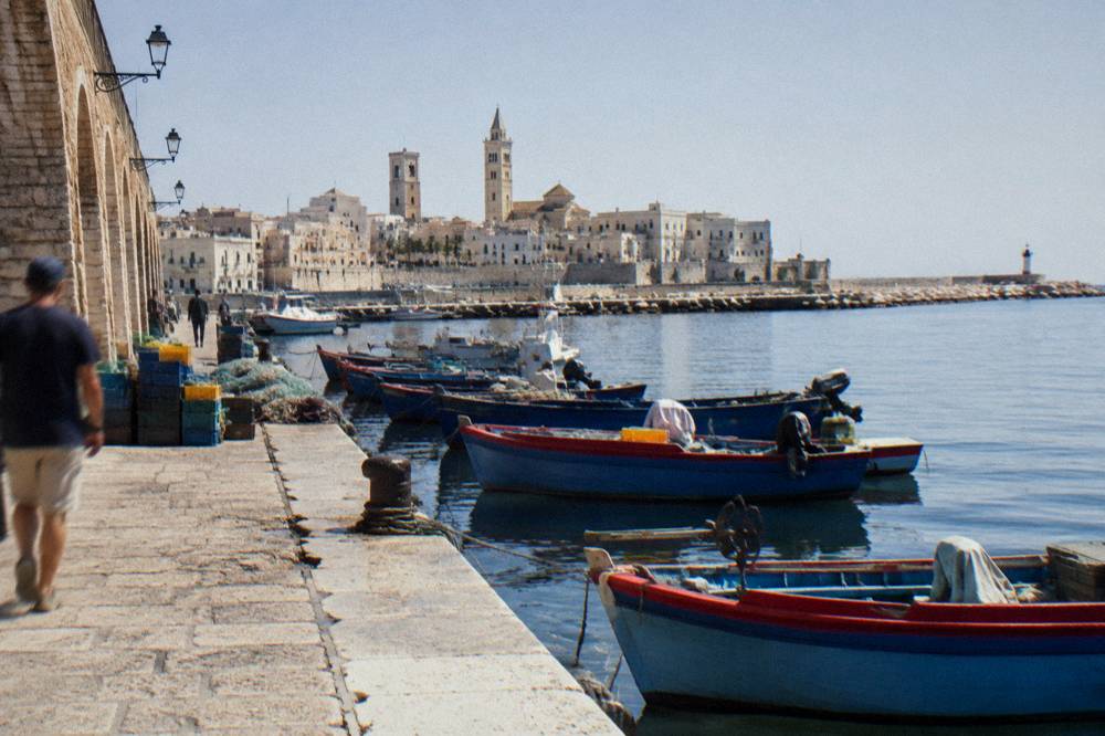 Old harbour pier with small wooden fishing boats, crates and nets and the pale old town skyline with two towers behind