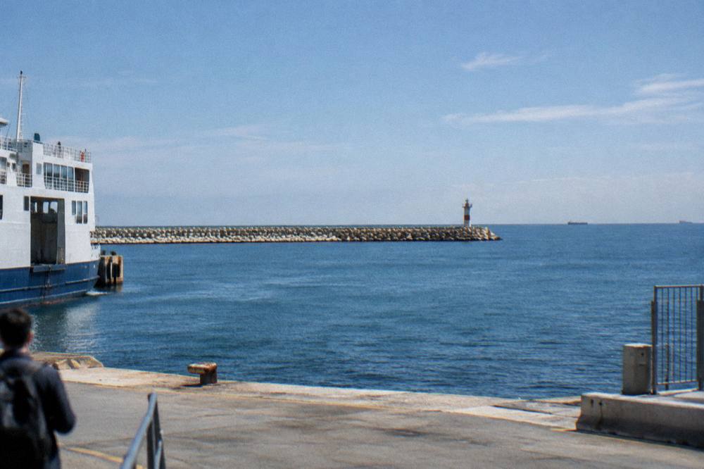 Long breakwater of concrete blocks with a small beacon at its end above the open Adriatic