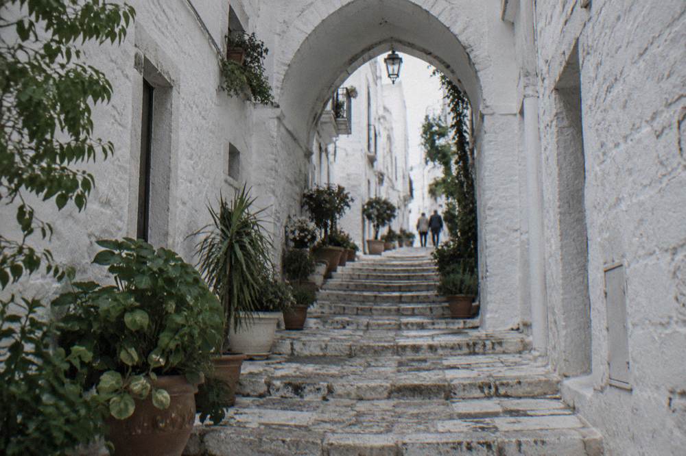 Steep whitewashed alley with stone steps, a pointed arch overhead and potted plants
