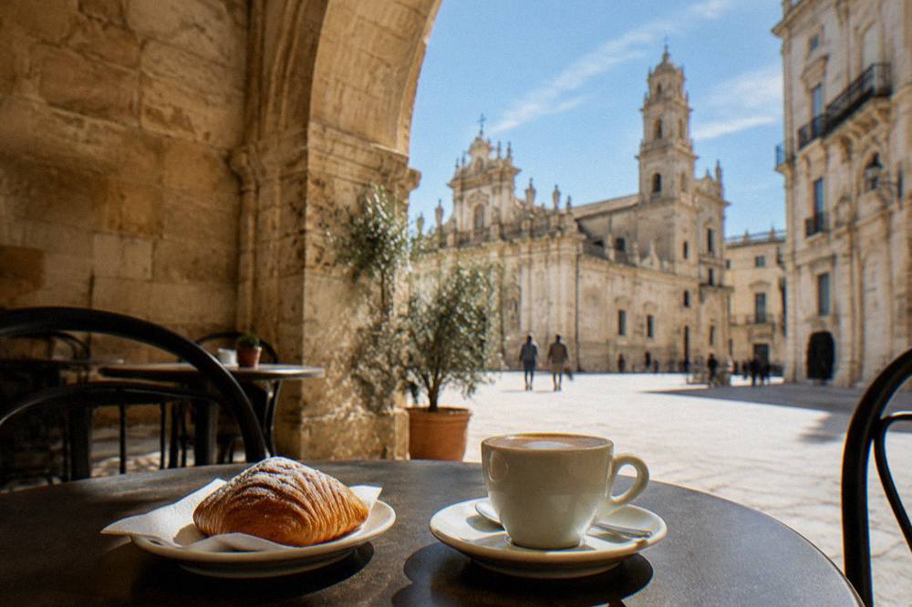 Cafe terrace under a stone arch with a cup of coffee and a pastry on a small table