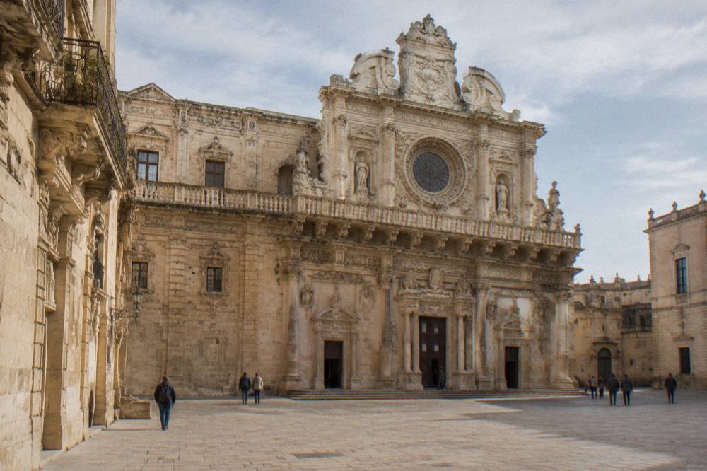 Richly carved baroque church facade of honey-coloured limestone with ornate balconies and a rose window