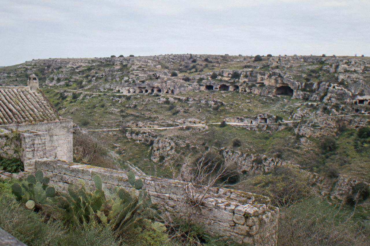 Rocky plateau across a ravine with scattered cave openings and sparse scrub in clear late light
