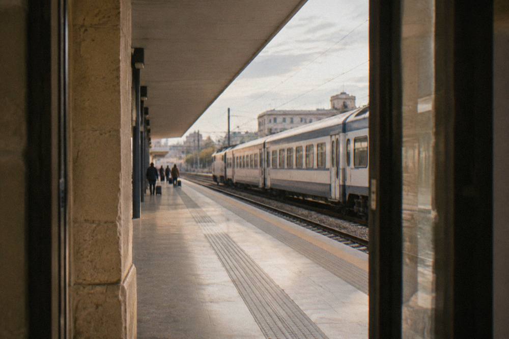 Regional train pulling into a station platform under a long canopy with a few distant waiting travellers