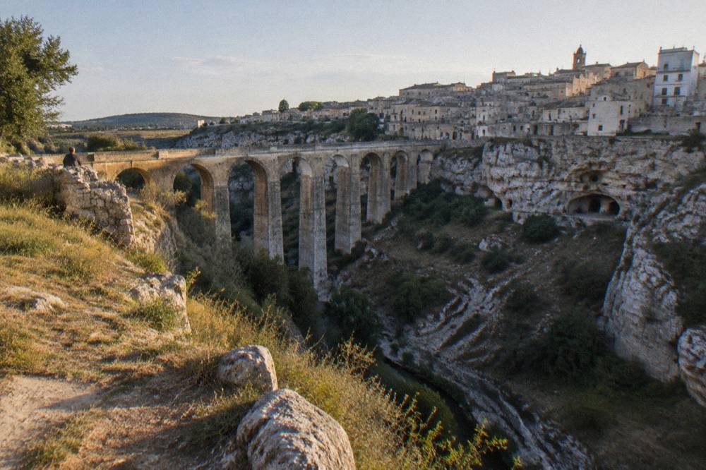 Deep rocky ravine crossed by a tall many-arched stone bridge with old town houses on the far rim