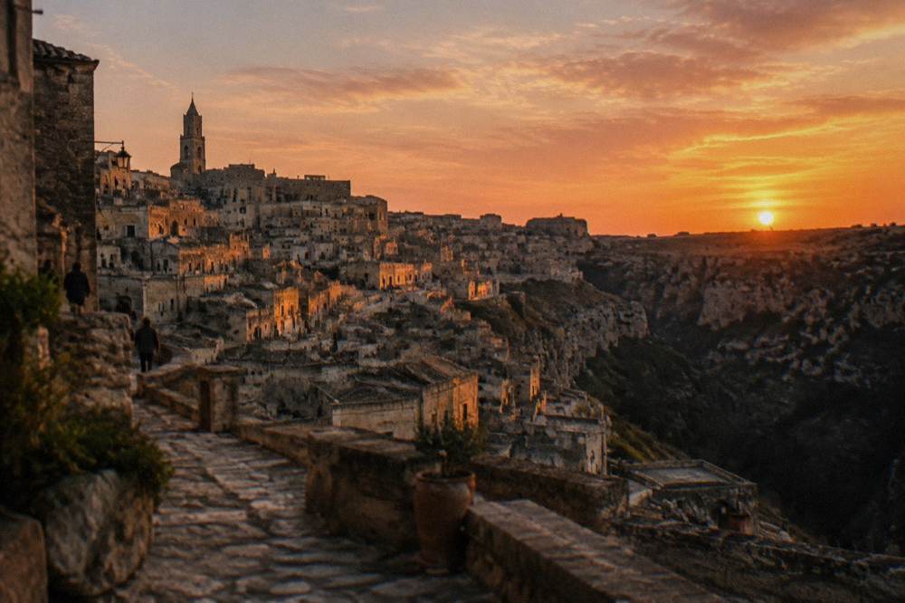 Sunset gold on stacked rooftops and cave facades of an ancient stone town above a shadowed ravine
