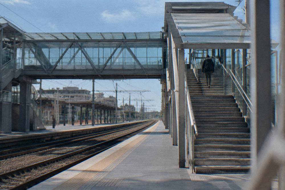 Station footbridge with stairs and a glass roof and a distant traveller with a rucksack