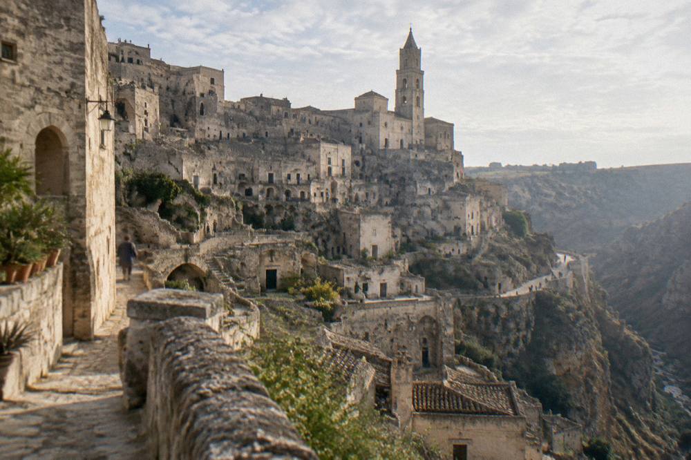Tiers of honey-coloured cave dwellings stacked on the side of a deep ravine below a cathedral bell tower