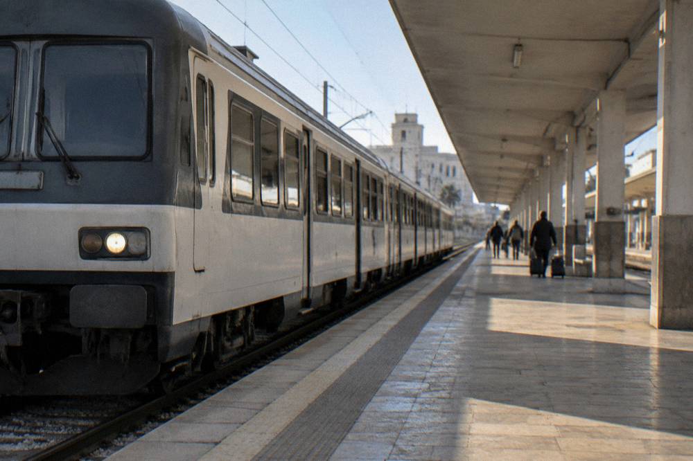 Regional train pulling into a station platform under a long canopy with a few distant waiting travellers