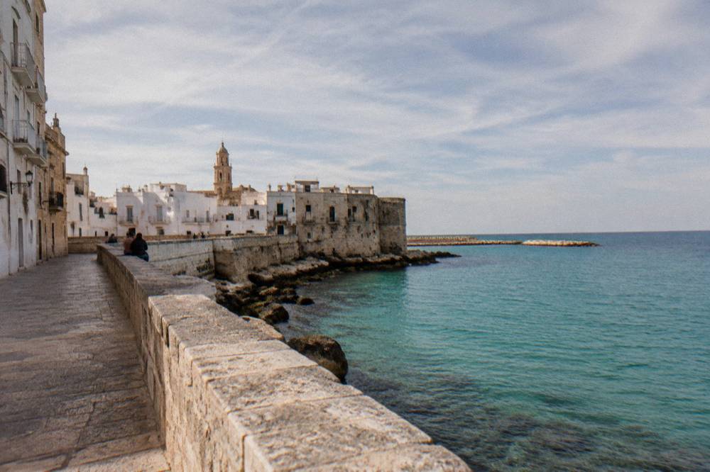 Sea promenade along an old town wall above calm turquoise water with distant people sitting on the wall