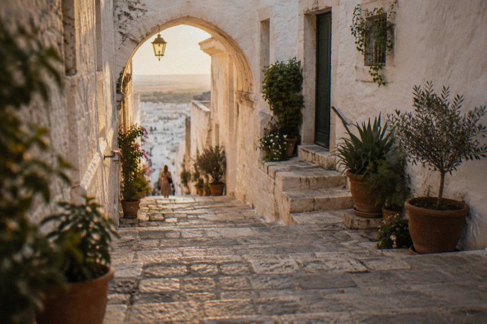 Steep whitewashed alley with stone steps, a pointed arch overhead and potted plants