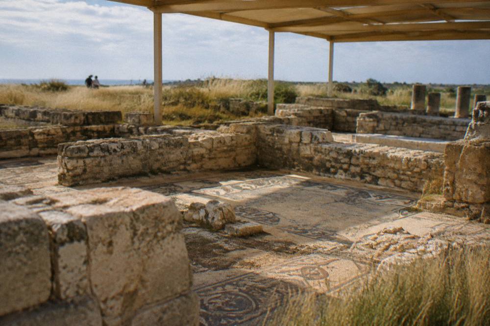 Stone foundations of an ancient basilica with patches of mosaic floor under a light shelter