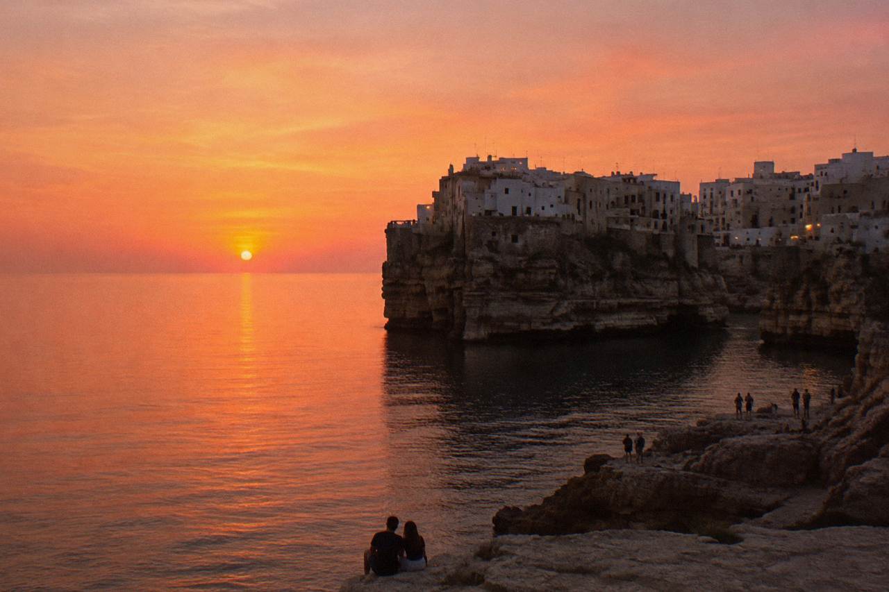 Cliff-top town in silhouette against a pink and orange sunset over a calm sea