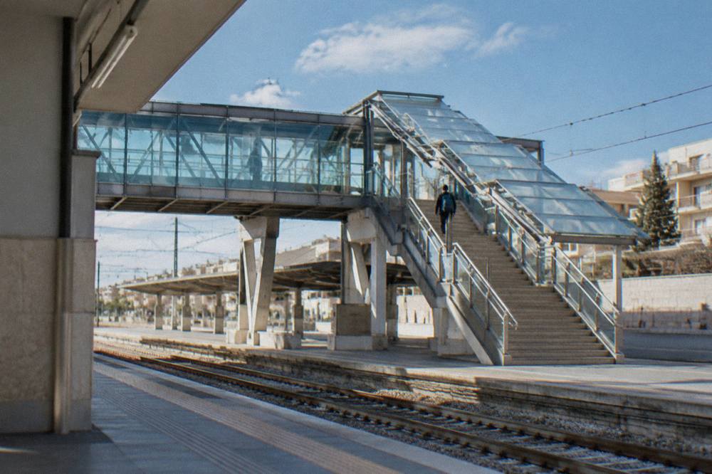 Station footbridge with stairs and a glass roof and a distant traveller with a rucksack