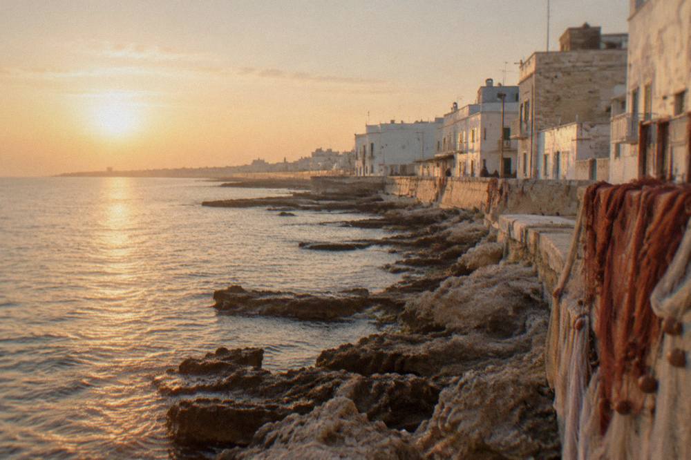 Rocky shore beside simple seafront houses with nets drying in hazy morning light