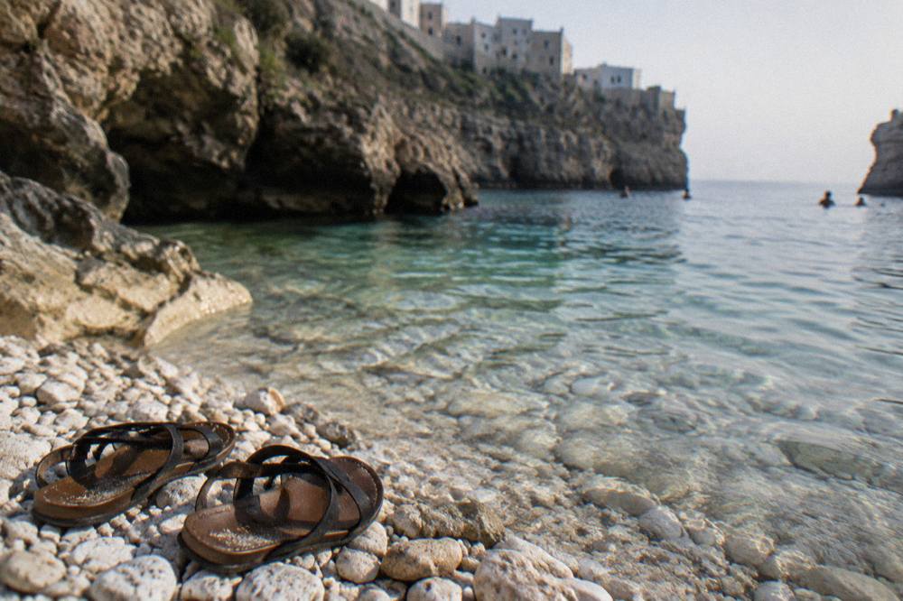 White pebbles and clear shallow water at the edge of a cove with a pair of sandals left on the stones
