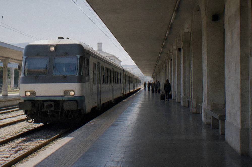 Regional train pulling into a station platform under a long canopy with a few distant waiting travellers