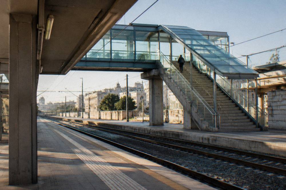 Station footbridge with stairs and a glass roof and a distant traveller with a rucksack