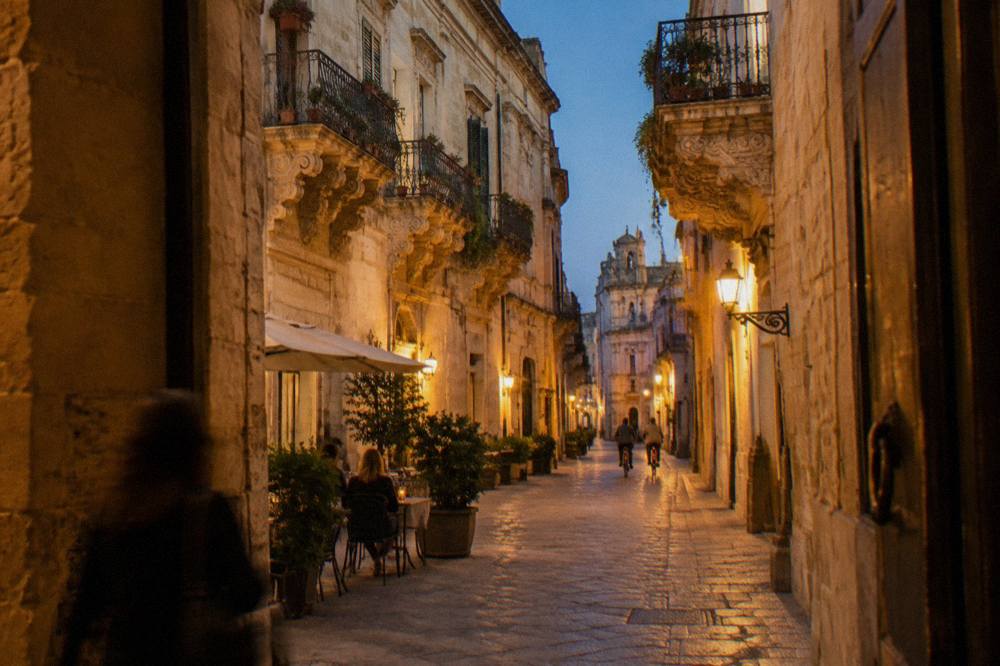 Narrow lane with baroque balconies on carved brackets in warm evening light and a cafe table
