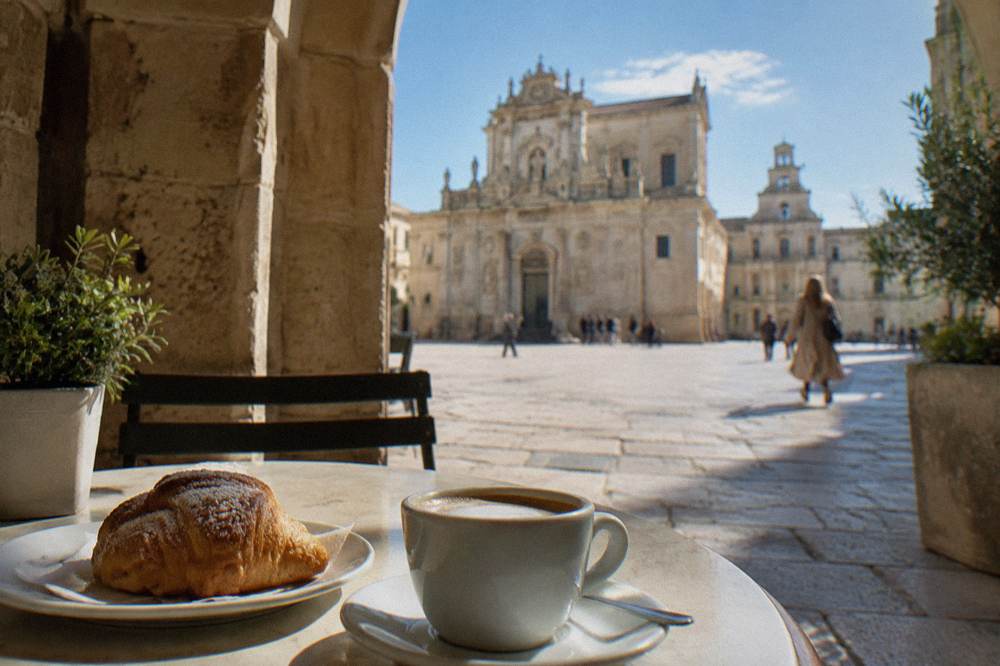 Cafe terrace under a stone arch with a cup of coffee and a pastry on a small table