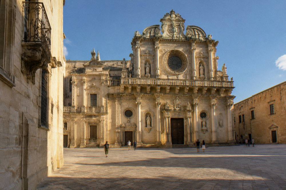 Richly carved baroque church facade of honey-coloured limestone with ornate balconies and a rose window