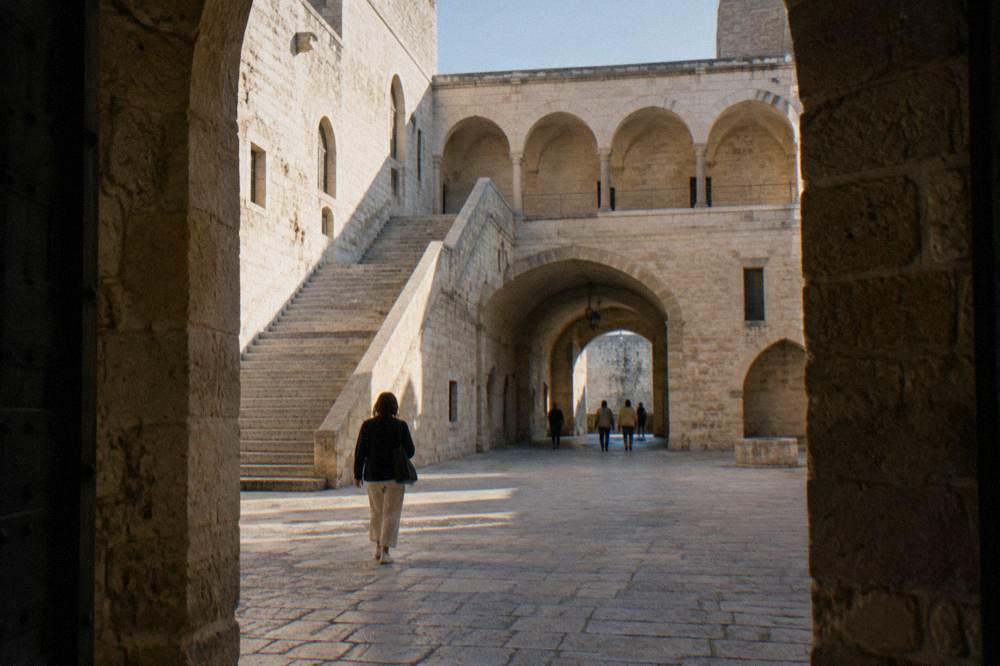 Inner courtyard of a medieval castle with a pale stone arcade, a broad staircase and a vaulted passage