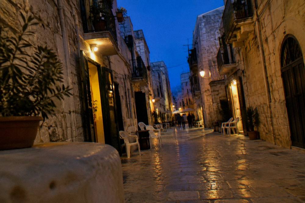 Old town lane at blue hour with warm light glowing from doorways and chairs set outside