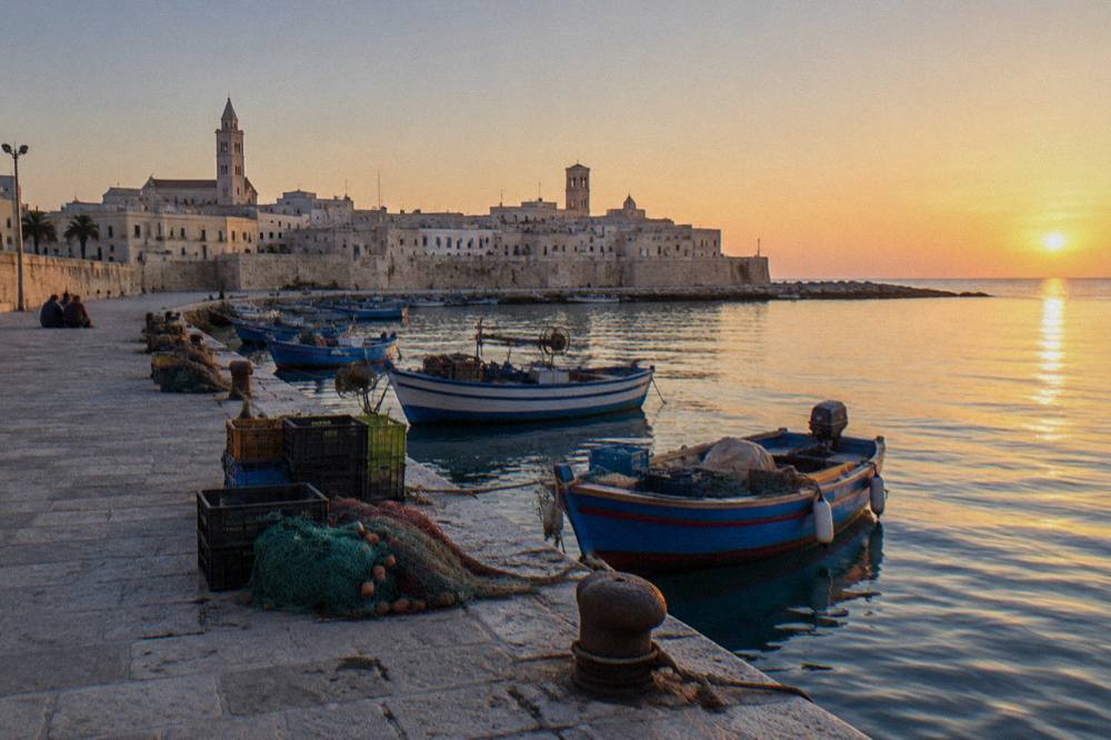 Old harbour pier with small wooden fishing boats, crates and nets and the pale old town skyline with two towers behind