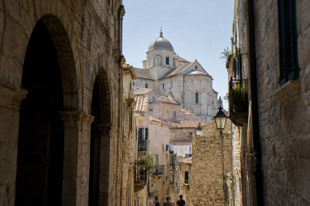 Cathedral dome and apse rising above terracotta rooftops at the end of a narrow old-town lane in afternoon light