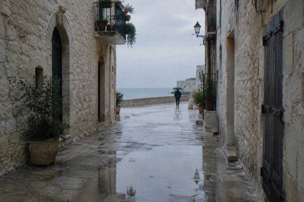 Wet limestone old town lane after rain with reflections in puddles and a distant person under an umbrella