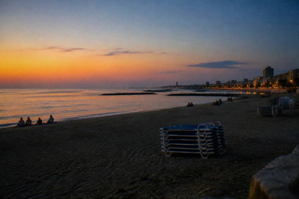 City beach in the evening with distant people on the sand, stacked sunbeds and an almost still sea