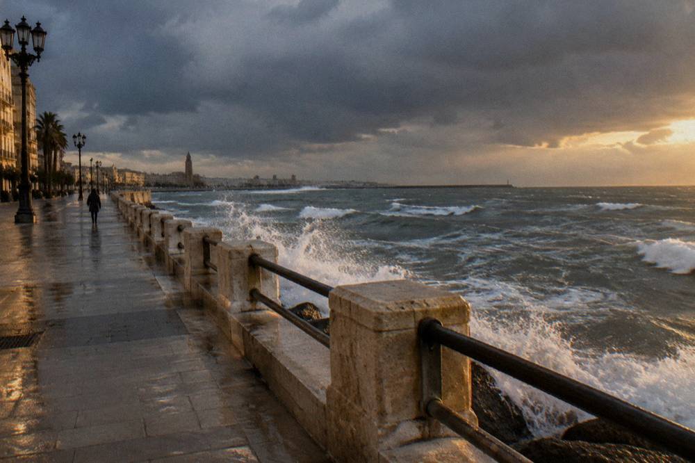 Grey winter sea with white-capped waves breaking against a seafront wall under a heavy sky