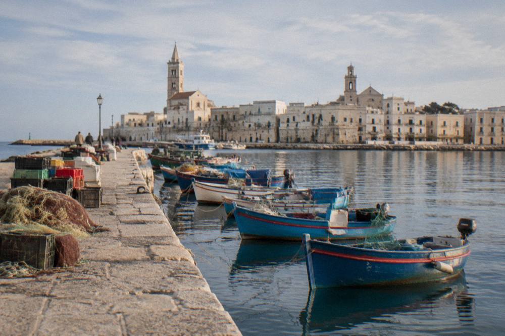 Old harbour pier with small wooden fishing boats, crates and nets and the pale old town skyline with two towers behind