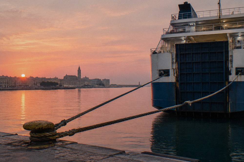 Stern of a ferry at a quay at sunrise with a pink sky, taut mooring ropes and still water