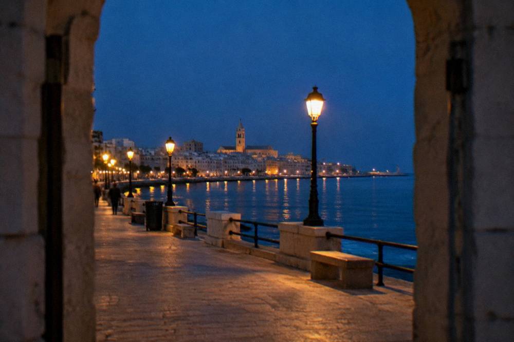Seafront promenade at blue hour with lit street lamps and the lights of the old town across the bay