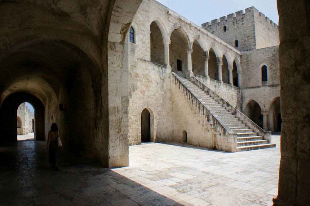 Inner courtyard of a medieval castle with a pale stone arcade, a broad staircase and a vaulted passage