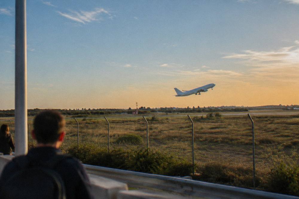 Plane taking off low over scrubby fields beyond a perimeter fence at golden hour