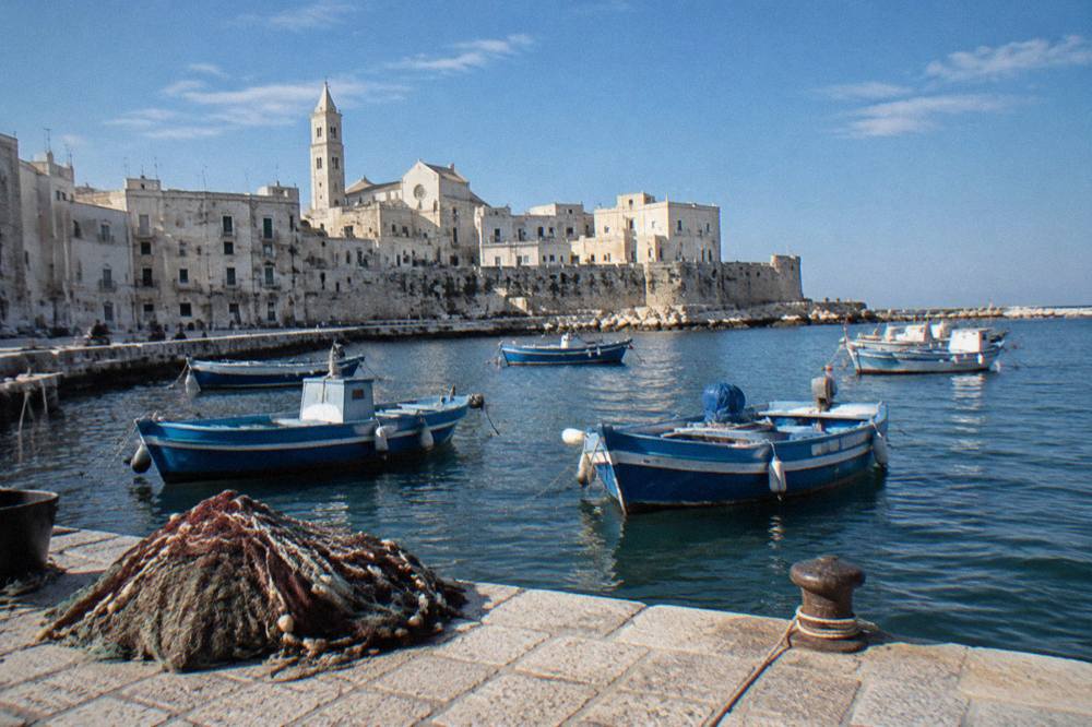 Small wooden fishing boats rocking at moorings with a net heap on the quay and pale old town walls behind