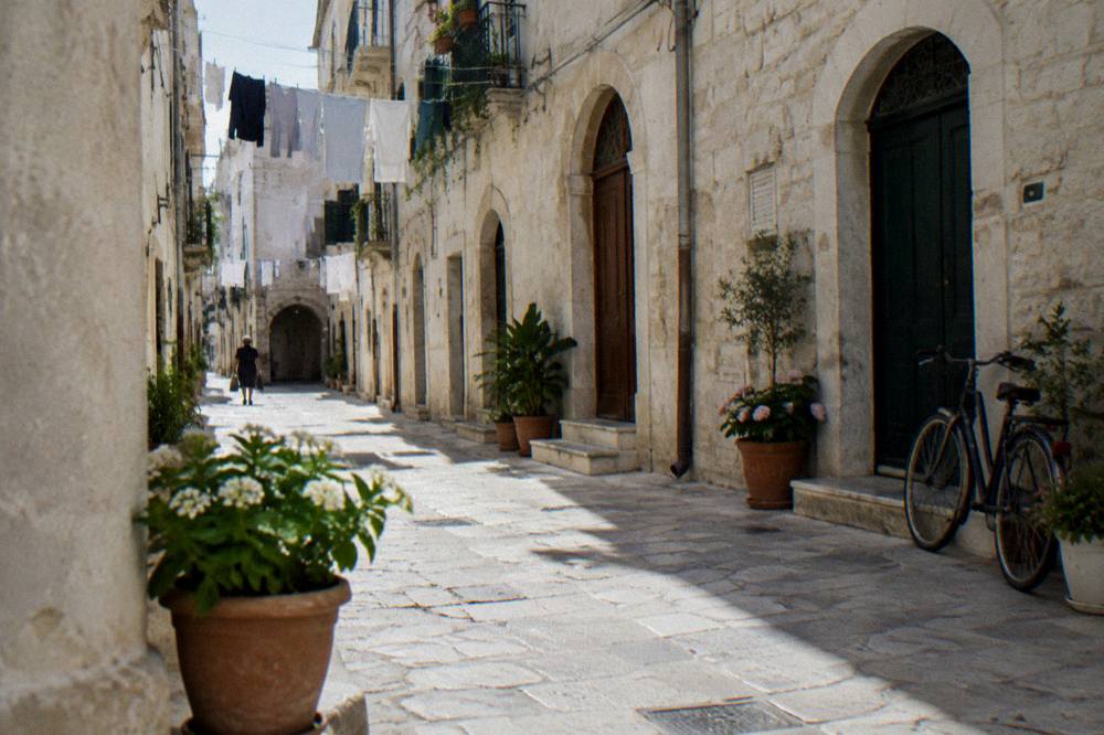 Narrow whitewashed old town lane with arched doorways, flower pots, washing overhead and a leaning bicycle in soft morning light