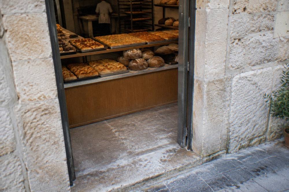 Neighbourhood bakery doorway with trays of golden focaccia and round loaves seen from the street