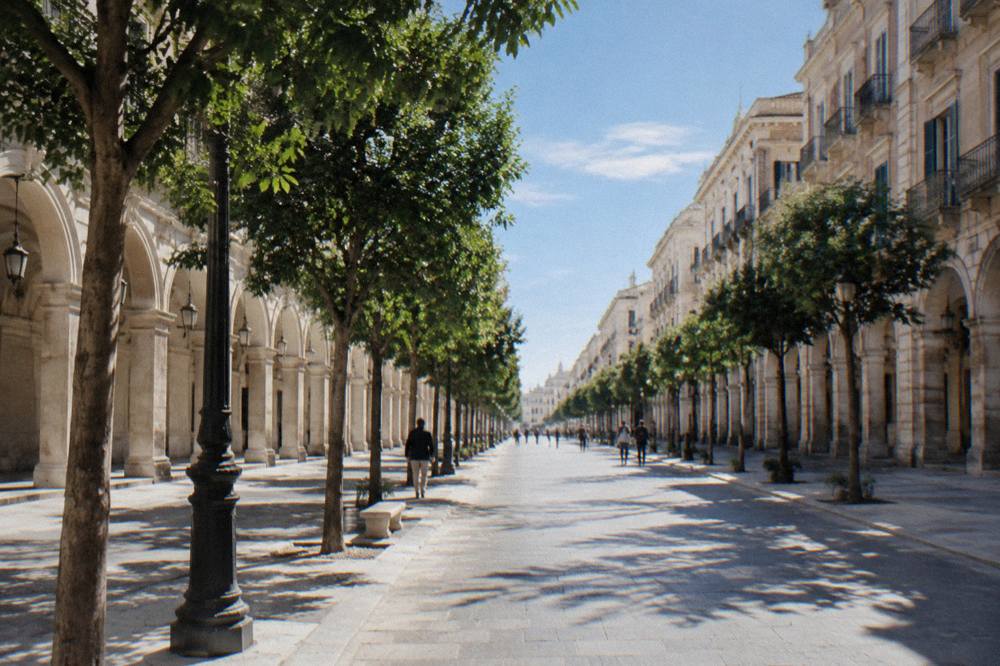 Long straight tree-lined boulevard of neoclassical buildings with arcaded ground floors